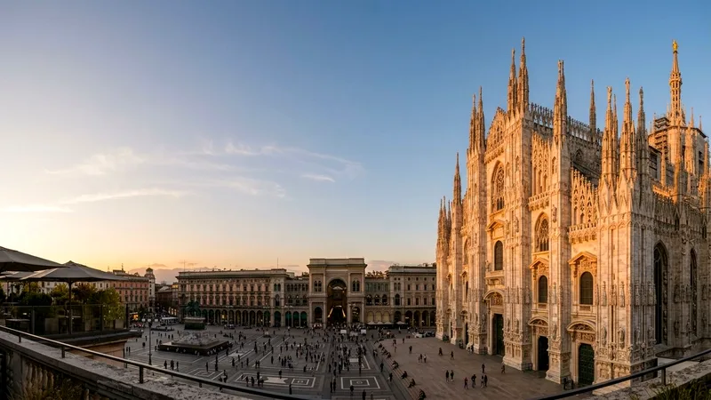 Milan Cathedral's white marble facade and spires glowing at golden hour over Piazza del Duomo.